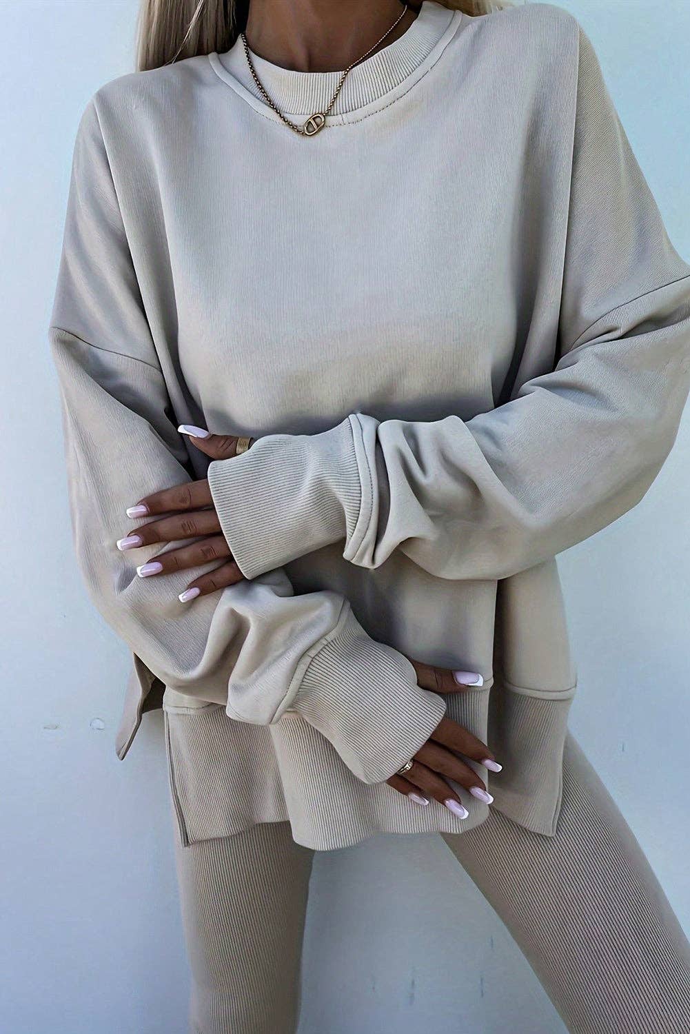 Person wearing a beige oversized sweatshirt and pants against a white background